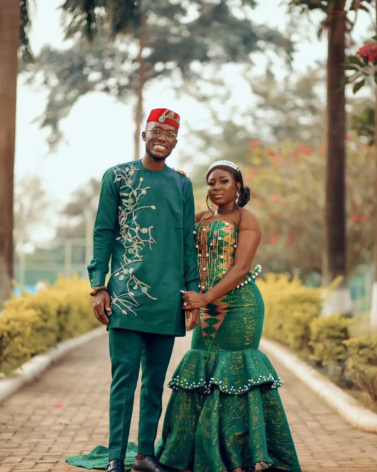 A newly married couple in green traditional dress, embroidered and beaded, on a path lined with palm trees